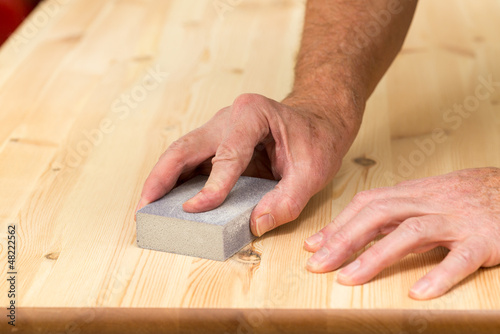 Photo: Mans hand on sanding block on pine wood Mans hand on sanding block on pine wood
