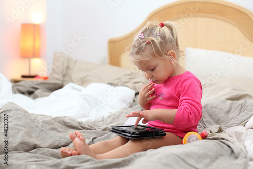 Photo: Toddler girl playing with tablet pc in bed Toddler girl playing with tablet pc in bed
