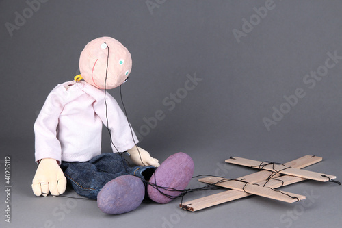 Photo: Wooden puppet sitting on grey background Wooden puppet sitting on grey background