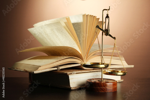 Photo: Gold scales of justice and books on brown background Gold scales of justice and books on brown background