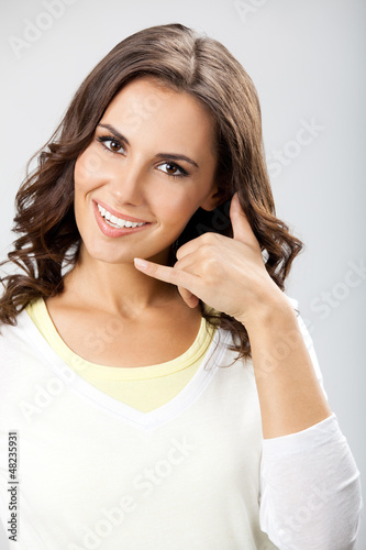 Photo: Young woman showing call me gesture, on gray Young woman showing call me gesture, on gray