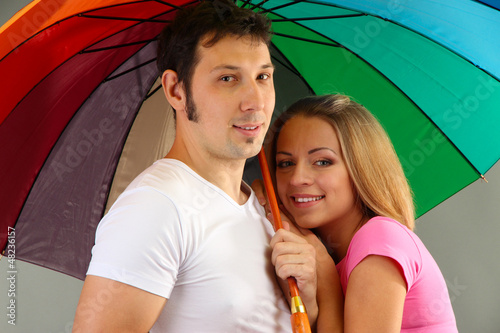 Photo: Loving couple with umbrella on grey background Loving couple with umbrella on grey background