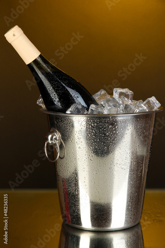 Photo: Bottle of wine in ice bucket on darck yellow background Bottle of wine in ice bucket on darck yellow background