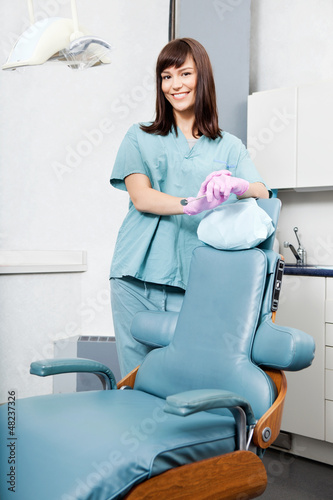 Photo: Smiling Female Dentist Standing By Dental Chair At Clinic Smiling Female Dentist Standing By Dental Chair At Clinic