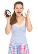 Stressed young woman in pajamas with ringing alarm clock