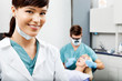 Photo: Female Hygienist With Dentist Working In The Background Female Hygienist With Dentist Working In The Background