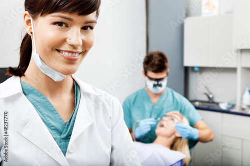 Photo: Female Hygienist With Dentist Working In The Background Female Hygienist With Dentist Working In The Background