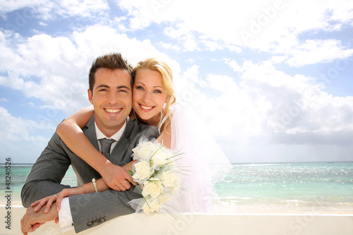 Photo: Just married couple leaning on fence by the beach Just married couple leaning on fence by the beach