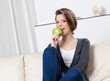 Sitting on the sofa attractive woman eats a green apple