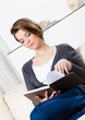 Beautiful woman reads the book sitting on the white leather sofa