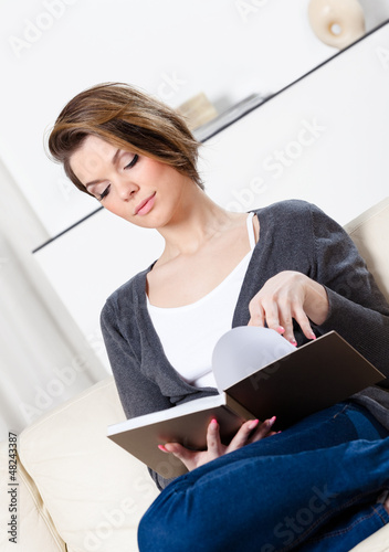 Photo: Beautiful woman reads the book sitting on the white leather sofa Beautiful woman reads the book sitting on the white leather sofa