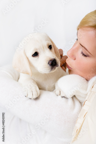 Photo: Woman in white sweater kissing white puppy of Labrador Woman in white sweater kissing white puppy of Labrador