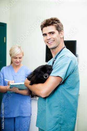 Photo: Veterinarian Doctor Carrying A Dog With Female Nurse Writing On Veterinarian Doctor Carrying A Dog With Female Nurse Writing On