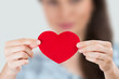 Young smiling woman holding red heart. Focus on heart