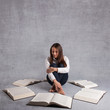 Photo: Young girl studying surrounded by books against grey background. Young girl studying surrounded by books against grey background.