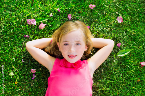 Photo: Blond kid girl lying on garden grass smiling aerial view Blond kid girl lying on garden grass smiling aerial view