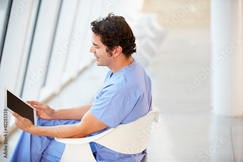 Photo: Male Nurse Sitting In Chair Using Digital Tablet Male Nurse Sitting In Chair Using Digital Tablet