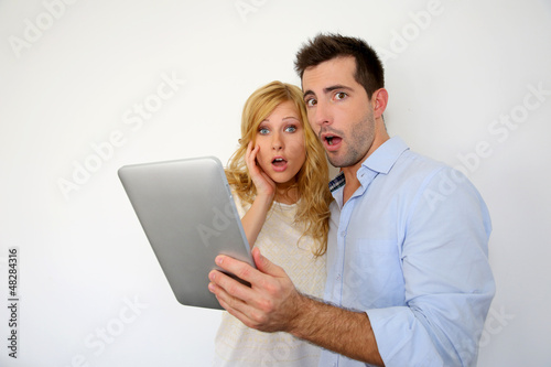 Photo: Couple with astonished expression in front of tablet Couple with astonished expression in front of tablet