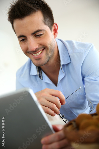 Photo: Cheerful young man websurfing on digital tablet at home Cheerful young man websurfing on digital tablet at home
