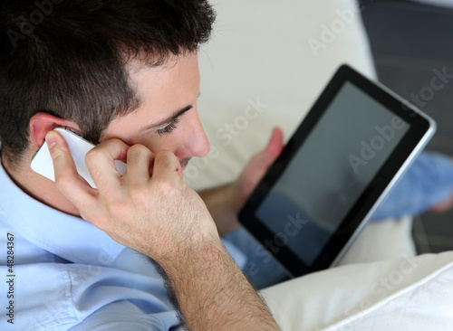 Photo: Man sitting in sofa using smartphone and tablet Man sitting in sofa using smartphone and tablet