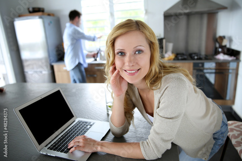 Photo: Cheerful blond girl connected on internet in home kitchen Cheerful blond girl connected on internet in home kitchen