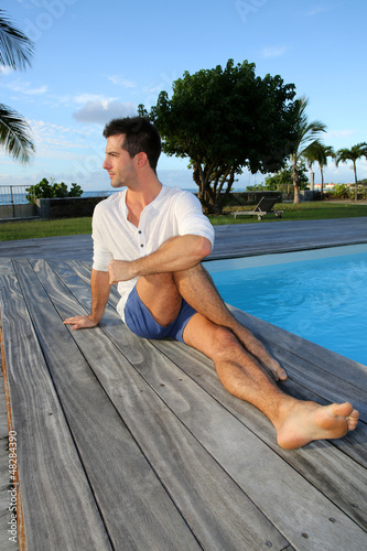 Photo: Young man doing stretching exercises on pool deck Young man doing stretching exercises on pool deck