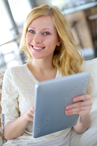Photo: Blond girl sitting in sofa with digital tablet Blond girl sitting in sofa with digital tablet