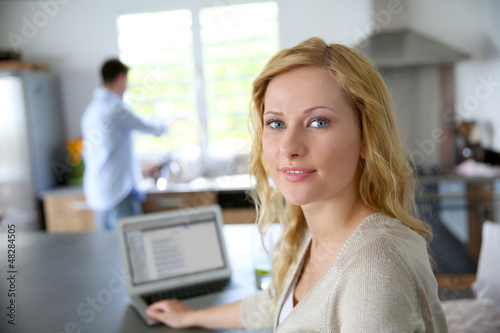 Photo: Cheerful blond girl connected on internet in home kitchen Cheerful blond girl connected on internet in home kitchen
