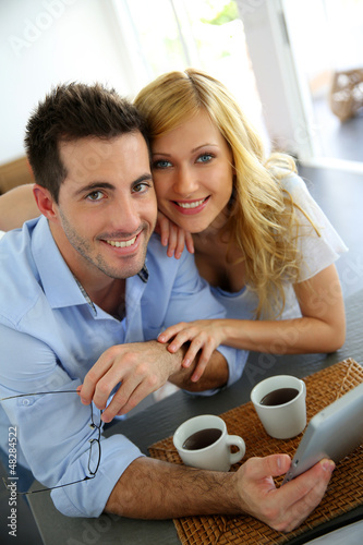 Photo: Young couple websurfing with tablet in home kitchen Young couple websurfing with tablet in home kitchen