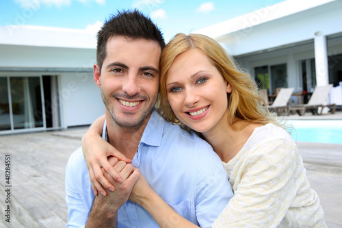 Photo: Cheerful young couple sitting in front of modern house Cheerful young couple sitting in front of modern house