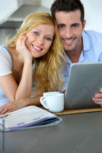 Photo: Young couple websurfing with tablet in home kitchen Young couple websurfing with tablet in home kitchen