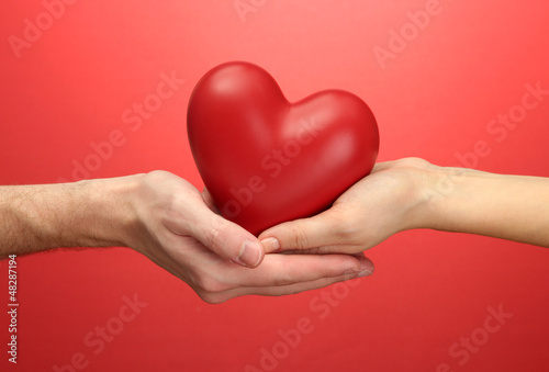 Photo: Red heart in woman and man hands, on red background Red heart in woman and man hands, on red background