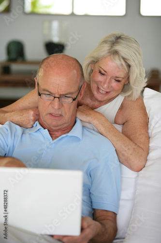 Photo: Senior couple sat on the sofa surfing the internet Senior couple sat on the sofa surfing the internet