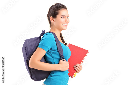 Photo: A female student with backpack walking and holding book A female student with backpack walking and holding book