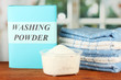 Box of washing powder with blue measuring cup and towels,