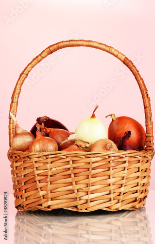 Photo: Ripe onions in basket on red background Ripe onions in basket on red background