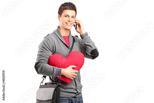 Photo: A smiling student holding a red heart and talking on a phone A smiling student holding a red heart and talking on a phone