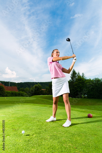 Photo: Young female golf player on course doing golf swing Young female golf player on course doing golf swing