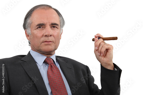 Photo: A mature businessman smoking a cigar. A mature businessman smoking a cigar.