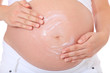 Schwangere Frau cremt ihren Bauch ein