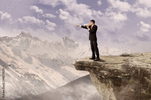 Photo: Businessman using speaker on cliff Businessman using speaker on cliff
