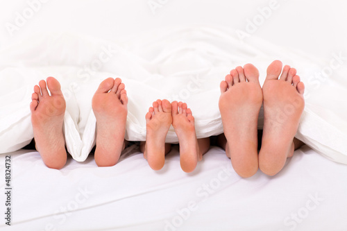 Photo: happy family of three lying under duvet on bed happy family of three lying under duvet on bed
