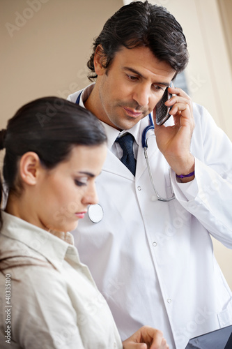 Photo: Doctor Attending Call While Standing With Colleague Doctor Attending Call While Standing With Colleague