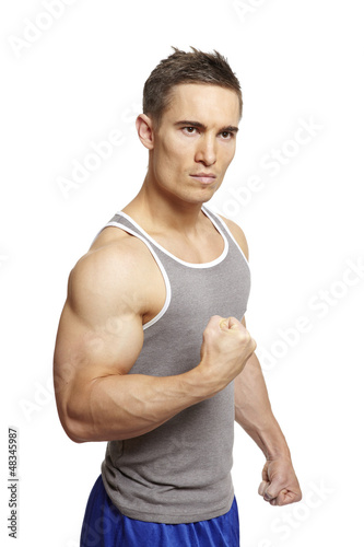 Photo: Muscular young man flexing arm muscles in sports outfit Muscular young man flexing arm muscles in sports outfit