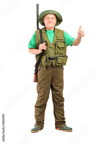 Photo: Full length portrait of a male hunter with shotgun giving a thum Full length portrait of a male hunter with shotgun giving a thum