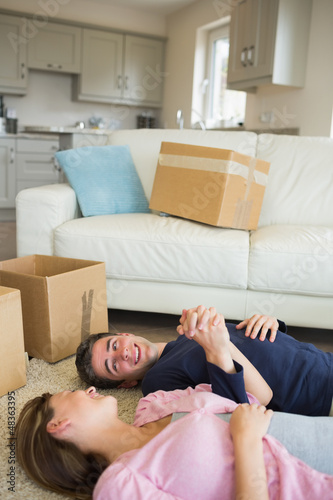Photo: Happy couple lying on floor with moving boxes Happy couple lying on floor with moving boxes
