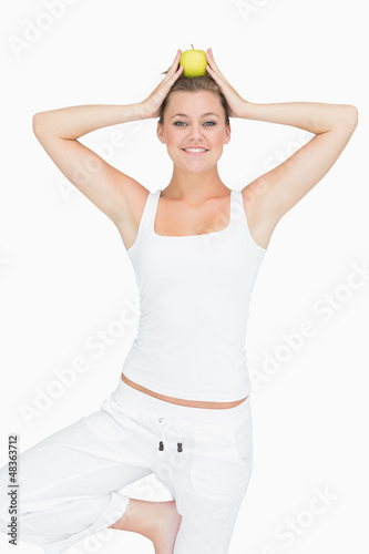 Photo: Woman doing yoga pose holding apple on her head Woman doing yoga pose holding apple on her head