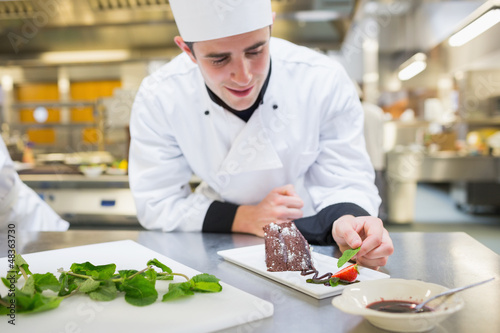 Photo: Cheerful chef putting mint with his dessert Cheerful chef putting mint with his dessert