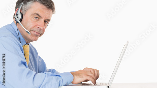Photo: Man writing on his laptop with headset Man writing on his laptop with headset