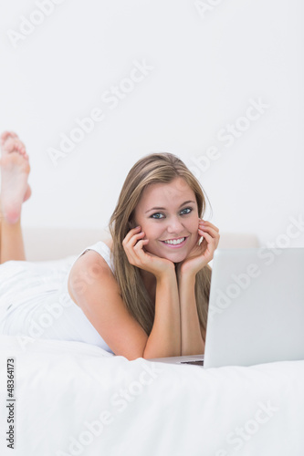Photo: Blonde woman lying on the bed with her laptop Blonde woman lying on the bed with her laptop